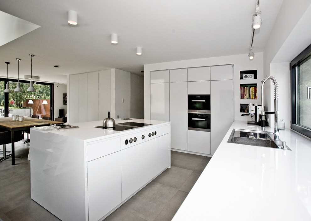 Large contemporary open plan kitchen in Stuttgart with a drop-in sink, flat-panel cabinets, white cabinets, black appliances and with island.