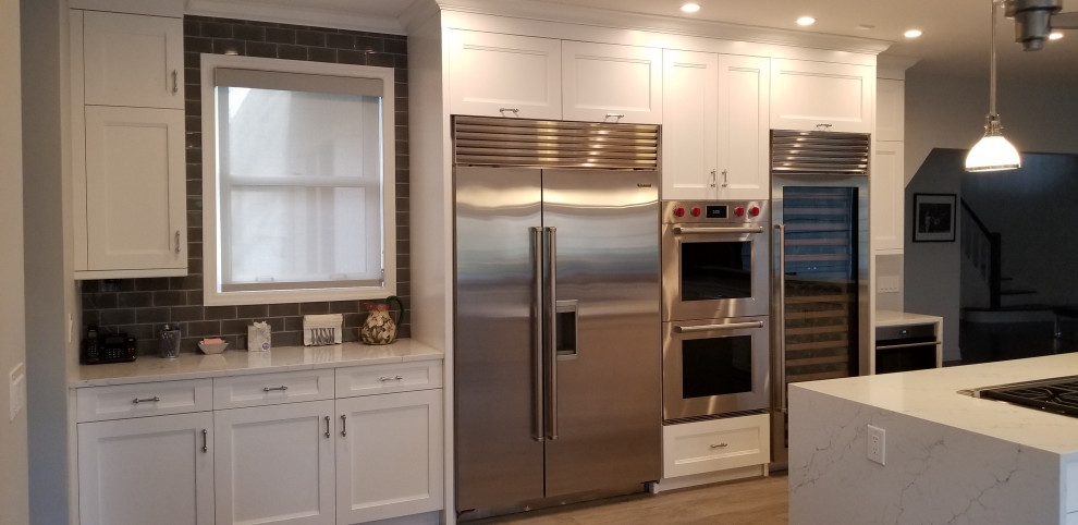Design ideas for a transitional u-shaped eat-in kitchen in New York with a farmhouse sink, recessed-panel cabinets, white cabinets, quartz benchtops, grey splashback, glass tile splashback, stainless steel appliances, porcelain floors, with island, brown floor and multi-coloured benchtop.