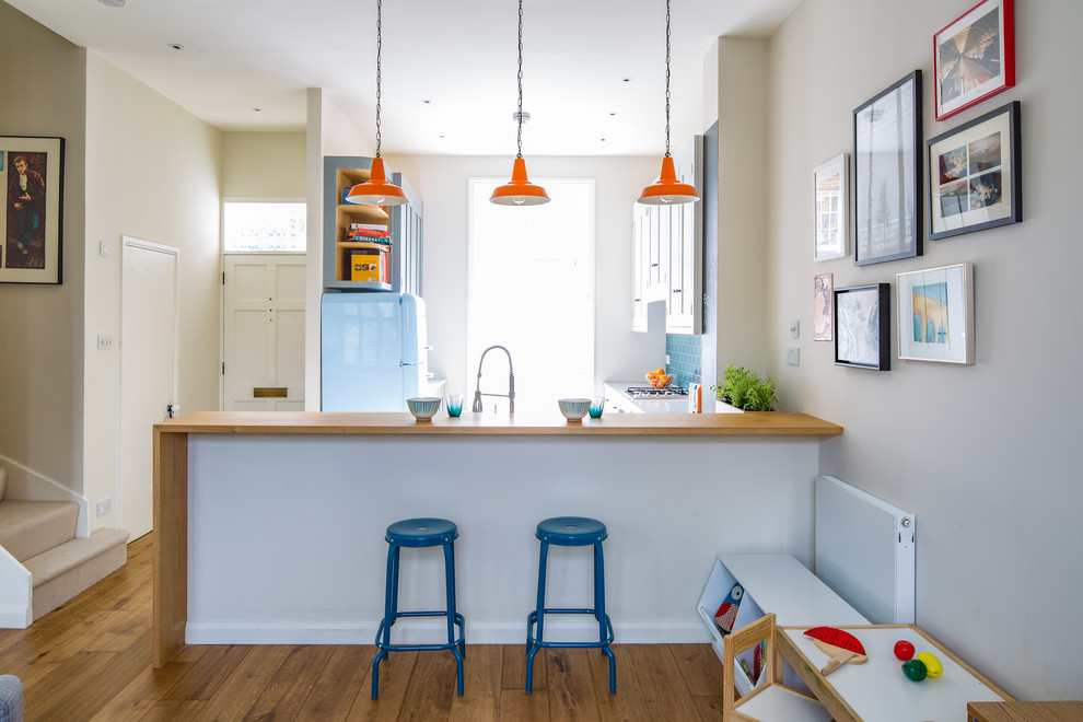 Photo of a small contemporary l-shaped open plan kitchen in London with a farmhouse sink, shaker cabinets, white cabinets, quartz benchtops, blue splashback, subway tile splashback, stainless steel appliances, ceramic floors, a peninsula and multi-coloured floor.