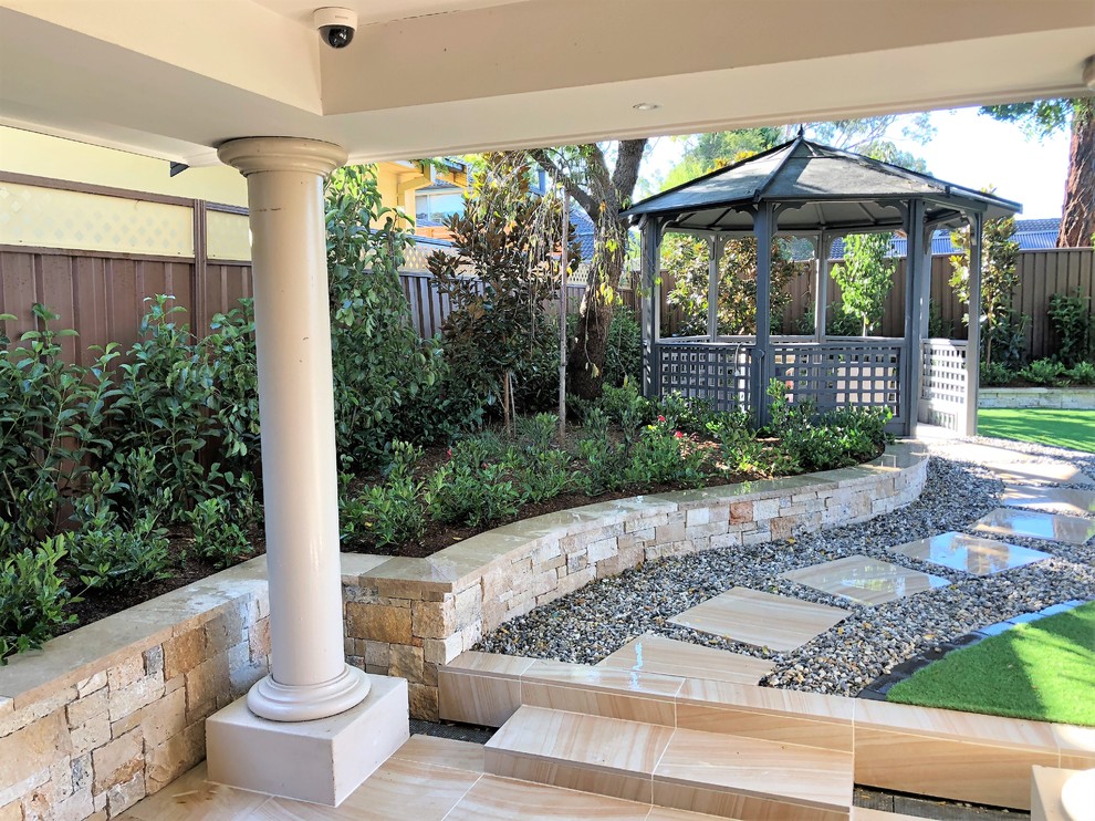 Design ideas for a mid-sized modern backyard full sun formal garden for summer in Sydney with a retaining wall and natural stone pavers.