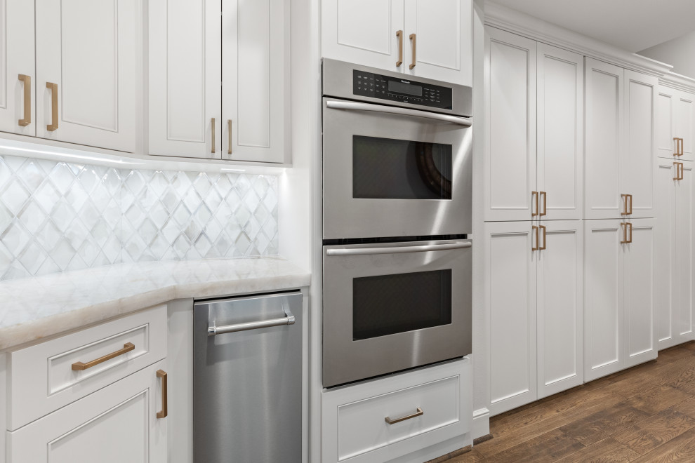 Eat-in kitchen - large transitional single-wall light wood floor and brown floor eat-in kitchen idea in Houston with a farmhouse sink, recessed-panel cabinets, white cabinets, quartzite countertops, white backsplash, mosaic tile backsplash, stainless steel appliances, an island and white countertops