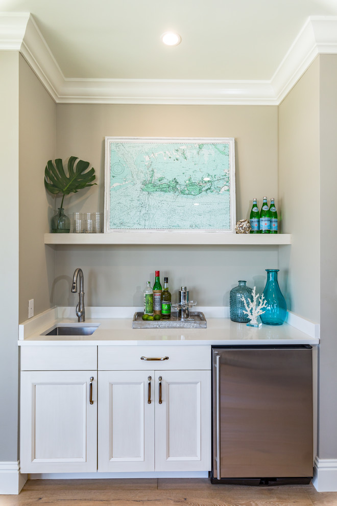 Design ideas for a beach style single-wall wet bar in Miami with an undermount sink, recessed-panel cabinets, white cabinets, light hardwood floors and white benchtop.