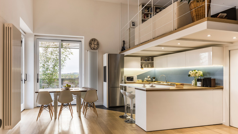 Large scandinavian u-shaped eat-in kitchen in Milan with a drop-in sink, flat-panel cabinets, white cabinets, wood benchtops, blue splashback, stainless steel appliances, porcelain floors, multiple islands and grey floor.