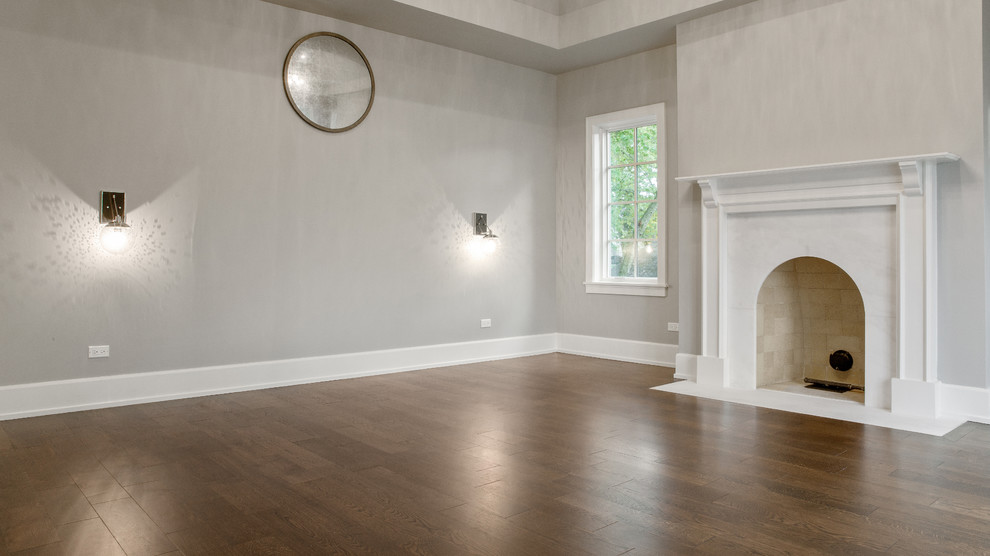 Réalisation d'un grand salon minimaliste fermé avec un mur gris, un sol en bois brun, une cheminée standard, un manteau de cheminée en pierre, un sol marron et un plafond voûté.