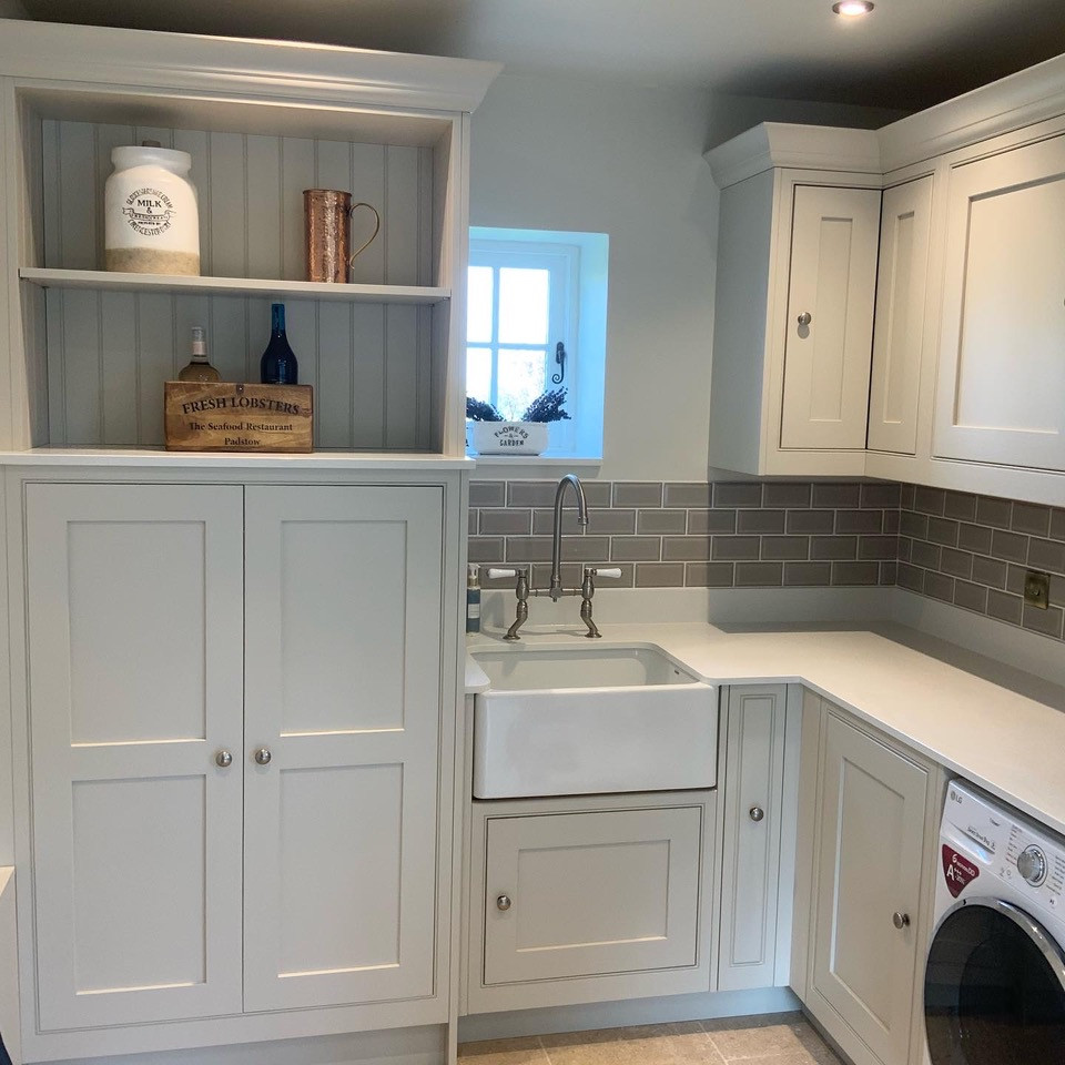 This is an example of a large laundry room in Buckinghamshire with a farmhouse sink, shaker cabinets, quartzite benchtops, grey splashback, ceramic splashback, beige floor and white benchtop.
