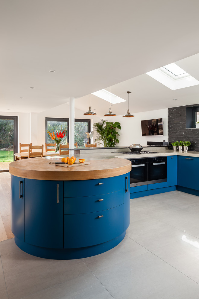 This is an example of a large industrial u-shaped eat-in kitchen in Other with a double-bowl sink, flat-panel cabinets, blue cabinets, concrete benchtops, metallic splashback, glass sheet splashback, stainless steel appliances and porcelain floors.