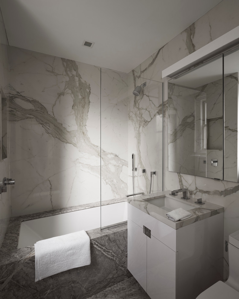 Photo of a mid-sized contemporary master bathroom in New York with flat-panel cabinets, white cabinets, an alcove tub, a shower/bathtub combo, white tile, grey walls, marble floors, a console sink and marble benchtops.