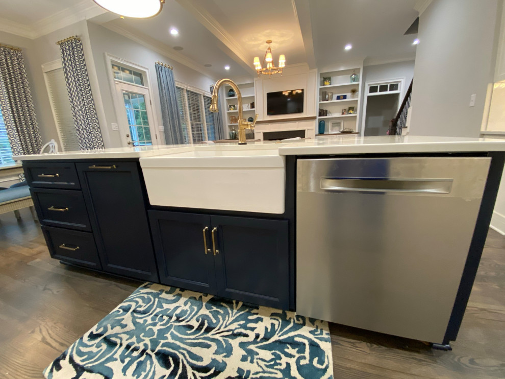 Mid-sized transitional single-wall open plan kitchen in Raleigh with a farmhouse sink, recessed-panel cabinets, white cabinets, white splashback, ceramic splashback, stainless steel appliances, dark hardwood floors, with island, brown floor, white benchtop and quartz benchtops.