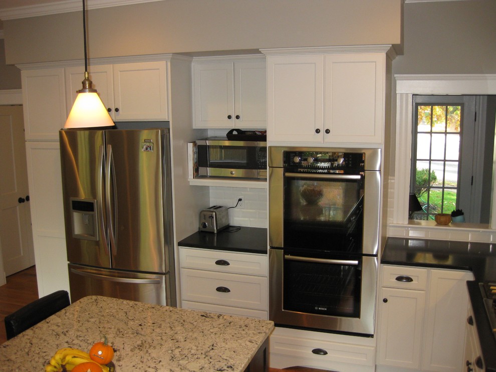 Transitional l-shaped medium tone wood floor eat-in kitchen photo in Boston with an undermount sink, shaker cabinets, white cabinets, granite countertops, white backsplash, ceramic backsplash, stainless steel appliances, an island and black countertops