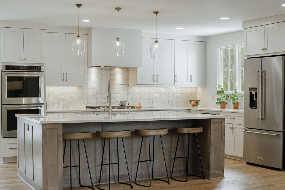 Design ideas for a large modern l-shaped eat-in kitchen in Other with a farmhouse sink, shaker cabinets, white cabinets, quartzite benchtops, white splashback, terra-cotta splashback, stainless steel appliances, light hardwood floors, with island, brown floor and white benchtop.