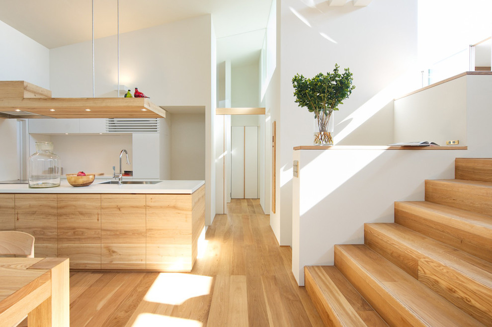 Design ideas for a scandinavian galley open plan kitchen in Other with an undermount sink, flat-panel cabinets, light wood cabinets, solid surface benchtops, white splashback, stainless steel appliances, light hardwood floors and with island.