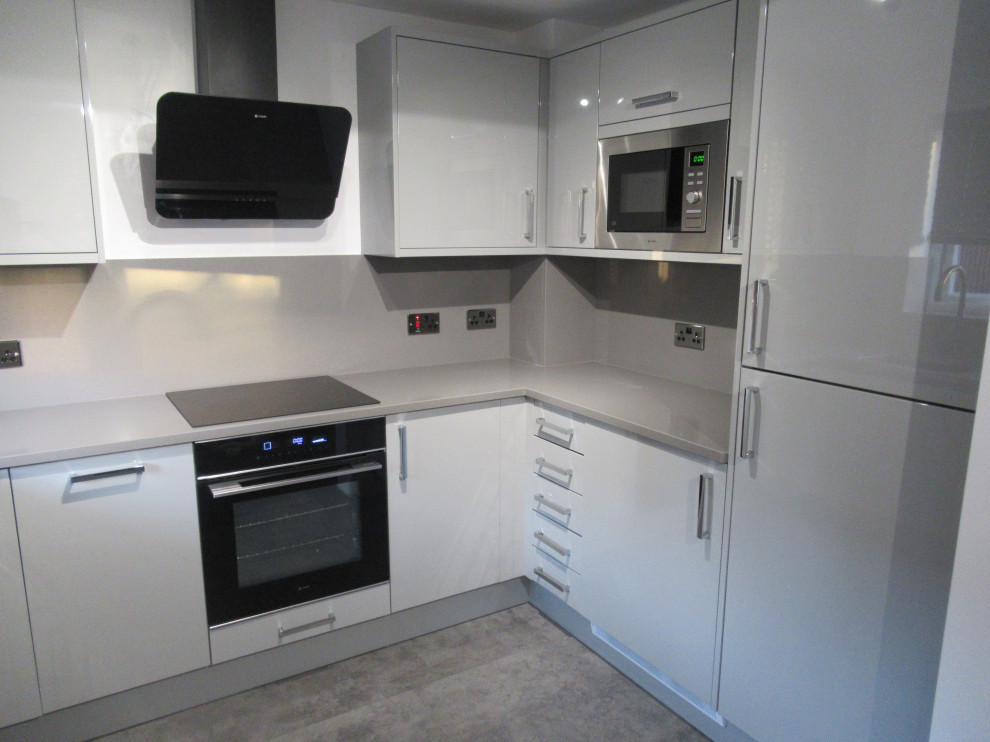 Small modern u-shaped eat-in kitchen in Other with an undermount sink, flat-panel cabinets, grey cabinets, quartzite benchtops, glass sheet splashback, black appliances, vinyl floors, no island, grey floor and grey benchtop.