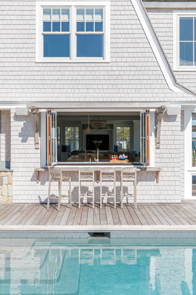 Large coastal side rectangular infinity swimming pool in Boston with a pool house and decking.