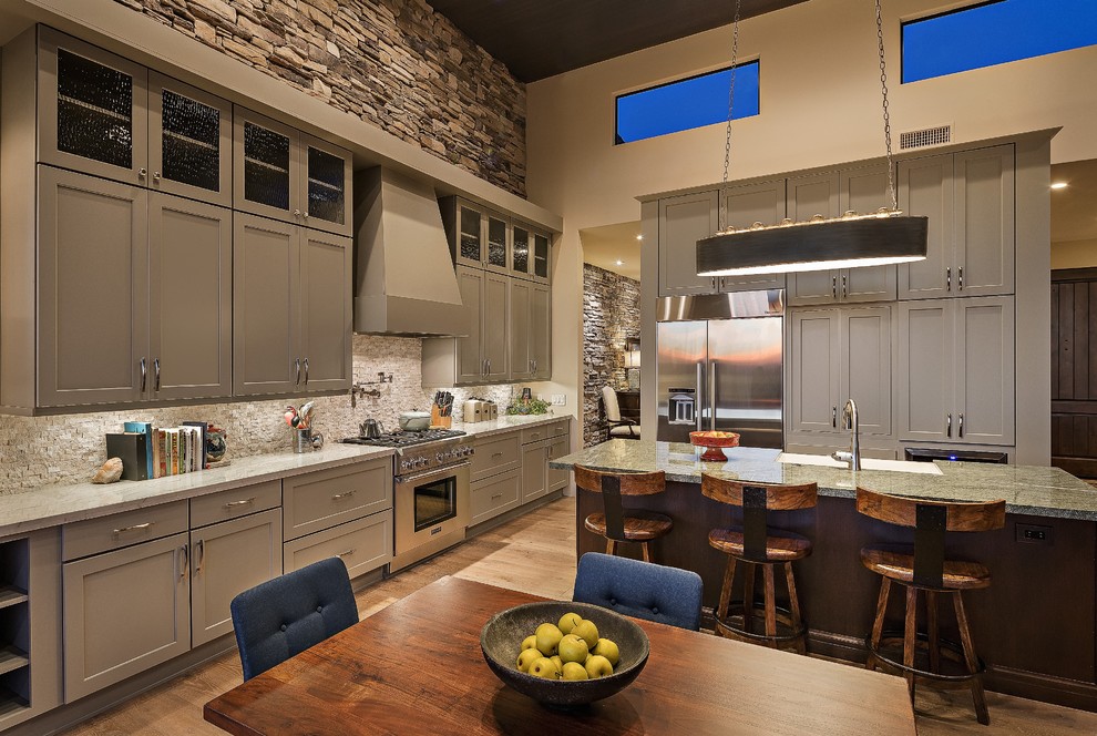 Eat-in kitchen - mid-sized rustic l-shaped light wood floor eat-in kitchen idea in Phoenix with a farmhouse sink, gray cabinets, granite countertops, beige backsplash, stone tile backsplash, stainless steel appliances and an island