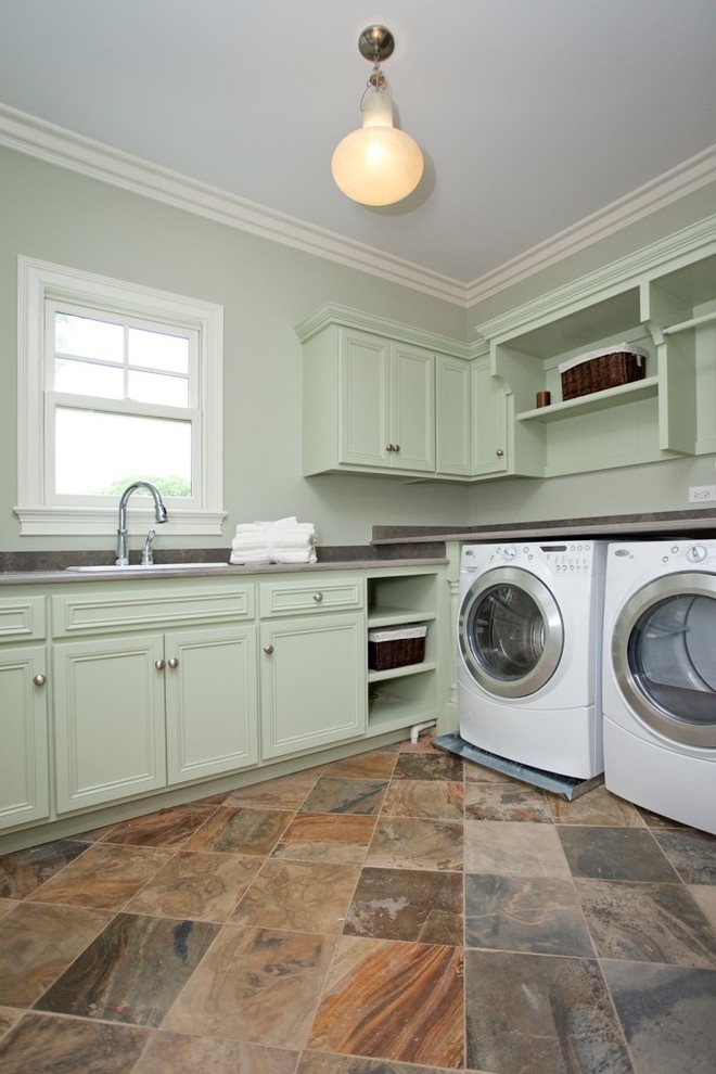 Mid-sized traditional l-shaped laundry room in Chicago with green cabinets, slate floors, a drop-in sink, recessed-panel cabinets, solid surface benchtops, a side-by-side washer and dryer, grey benchtop and grey walls.