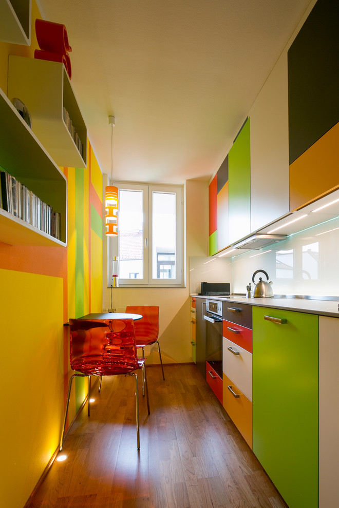 Small contemporary single-wall separate kitchen in Munich with flat-panel cabinets, white splashback, glass sheet splashback, black appliances, medium hardwood floors, no island and brown floor.