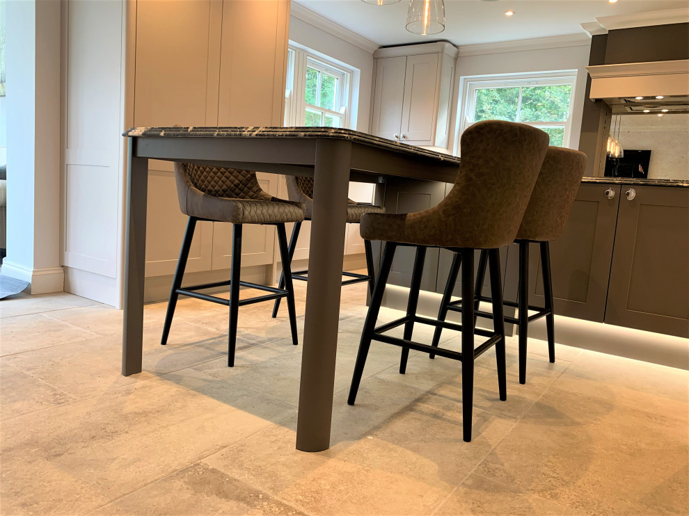 Mid-sized traditional l-shaped eat-in kitchen in Other with a farmhouse sink, shaker cabinets, medium wood cabinets, granite benchtops, black splashback, glass sheet splashback, black appliances, travertine floors, with island and black benchtop.