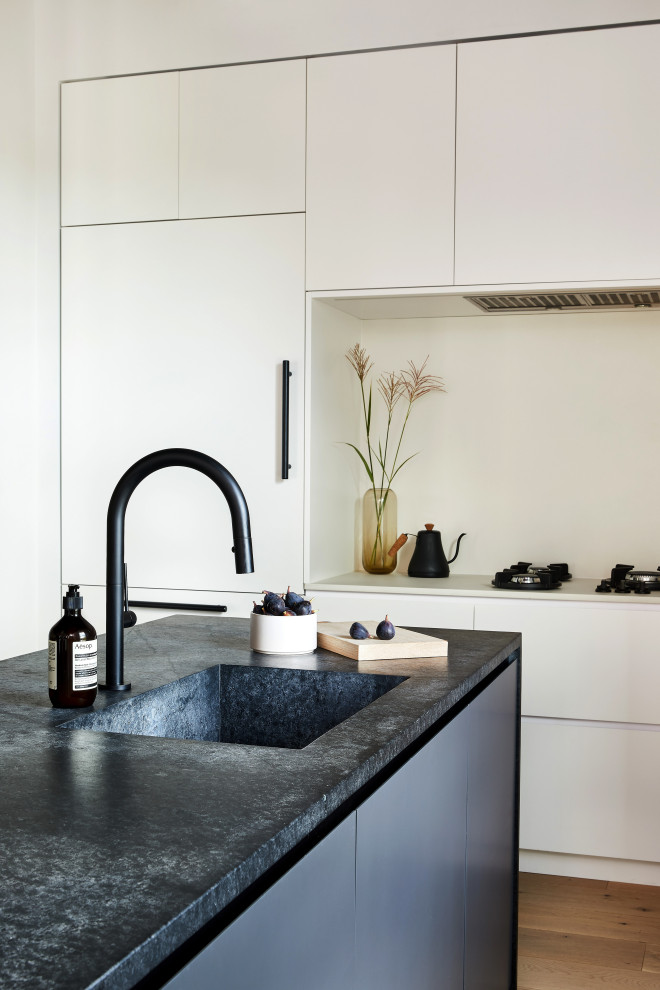 Modern kitchen in New York with an integrated sink, flat-panel cabinets, white cabinets, soapstone benchtops, white splashback, engineered quartz splashback, panelled appliances, white benchtop and exposed beam.