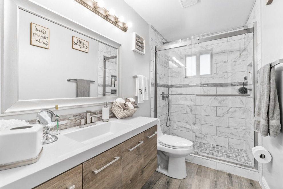 Photo of a mid-sized modern 3/4 bathroom in Miami with light wood cabinets, an alcove shower, a one-piece toilet, ceramic tile, grey walls, laminate floors, quartzite benchtops, beige floor, a sliding shower screen, white benchtops, a single vanity and a floating vanity.