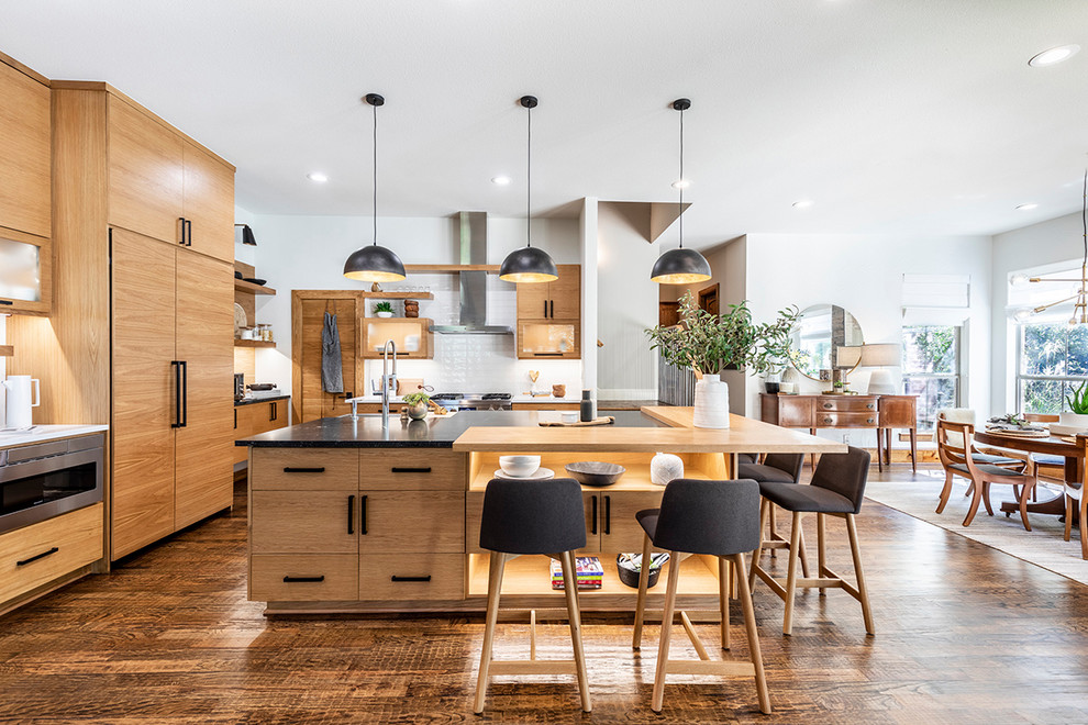 Inspiration for a scandinavian eat-in kitchen in Dallas with light wood cabinets, white splashback, dark hardwood floors, with island, black benchtop, flat-panel cabinets, panelled appliances and brown floor.