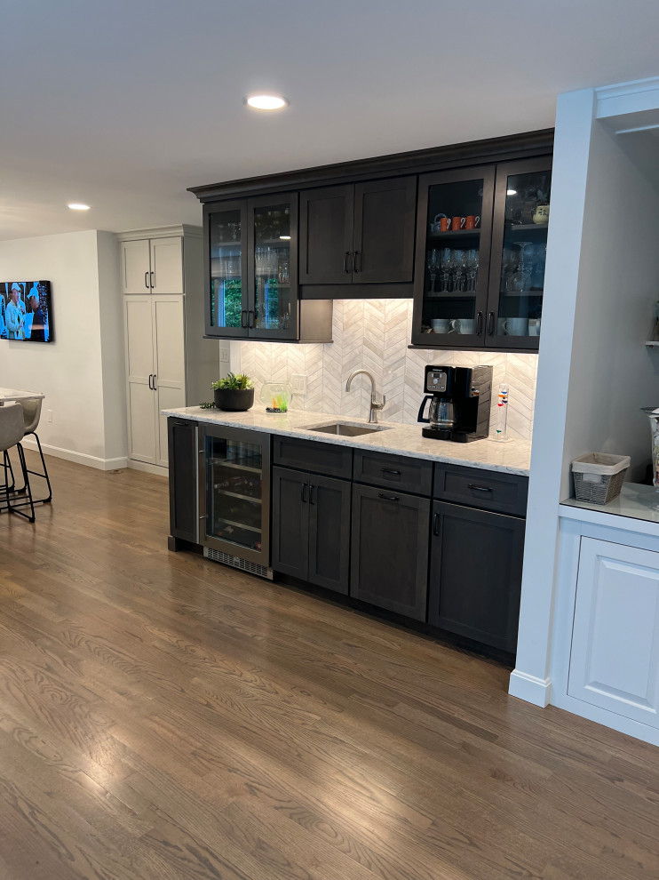 Design ideas for a mid-sized transitional single-wall wet bar in Boston with an undermount sink, recessed-panel cabinets, grey cabinets, quartz benchtops, white splashback, glass tile splashback, medium hardwood floors, grey floor and white benchtop.