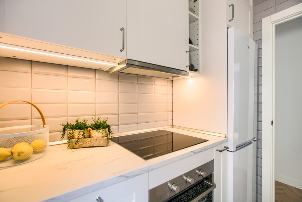 This is an example of a small midcentury grey and white galley enclosed kitchen in Madrid with a single-bowl sink, shaker cabinets, white cabinets, laminate countertops, grey splashback, ceramic splashback, white appliances, ceramic flooring, no island, grey floors and white worktops.