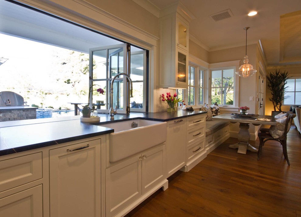 This is an example of a mid-sized traditional single-wall eat-in kitchen in Phoenix with a farmhouse sink, recessed-panel cabinets, white cabinets, marble benchtops, stainless steel appliances, dark hardwood floors, with island and brown floor.