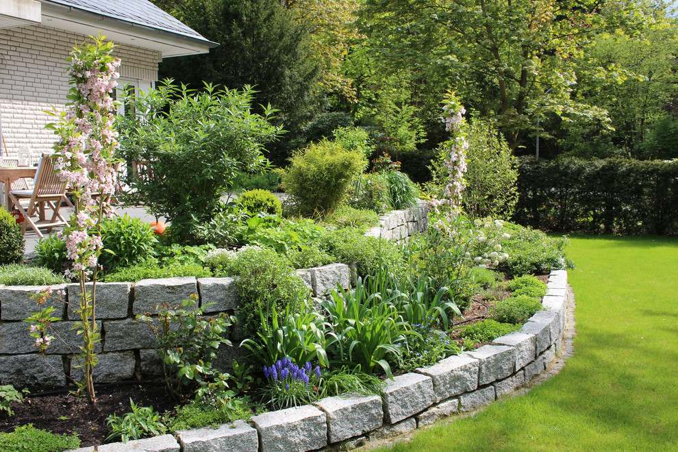 Large country full sun garden in Hamburg with a retaining wall and natural stone pavers for summer.
