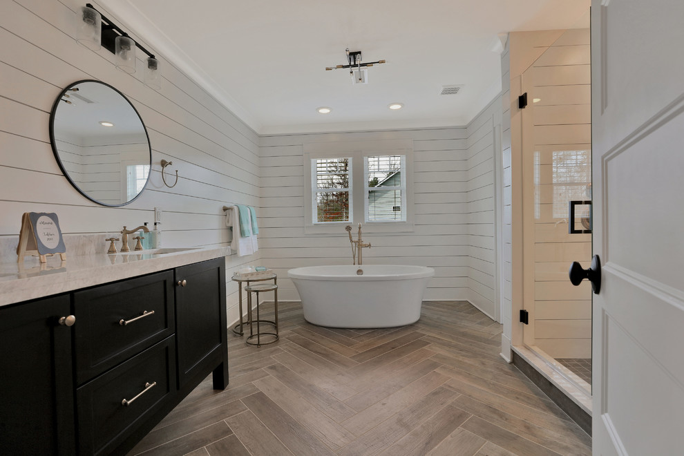 Country master bathroom in Richmond with shaker cabinets, black cabinets, a freestanding tub, an alcove shower, a one-piece toilet, white tile, multi-coloured walls, light hardwood floors, a pedestal sink, marble benchtops, beige floor and a hinged shower door.