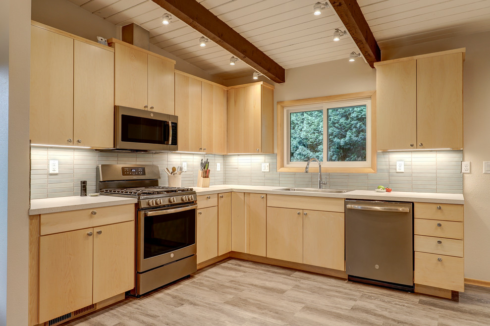 Photo of a mid-sized midcentury l-shaped eat-in kitchen in Portland with a drop-in sink, flat-panel cabinets, light wood cabinets, laminate benchtops, blue splashback, subway tile splashback, stainless steel appliances, light hardwood floors, no island and white benchtop.