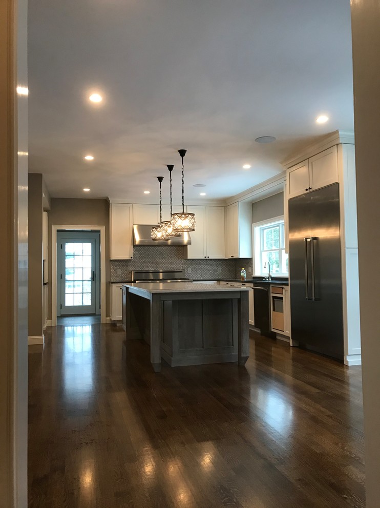 This is an example of a mid-sized tropical u-shaped separate kitchen in Boston with an undermount sink, shaker cabinets, white cabinets, solid surface benchtops, grey splashback, stainless steel appliances, dark hardwood floors, with island, brown floor and black benchtop.