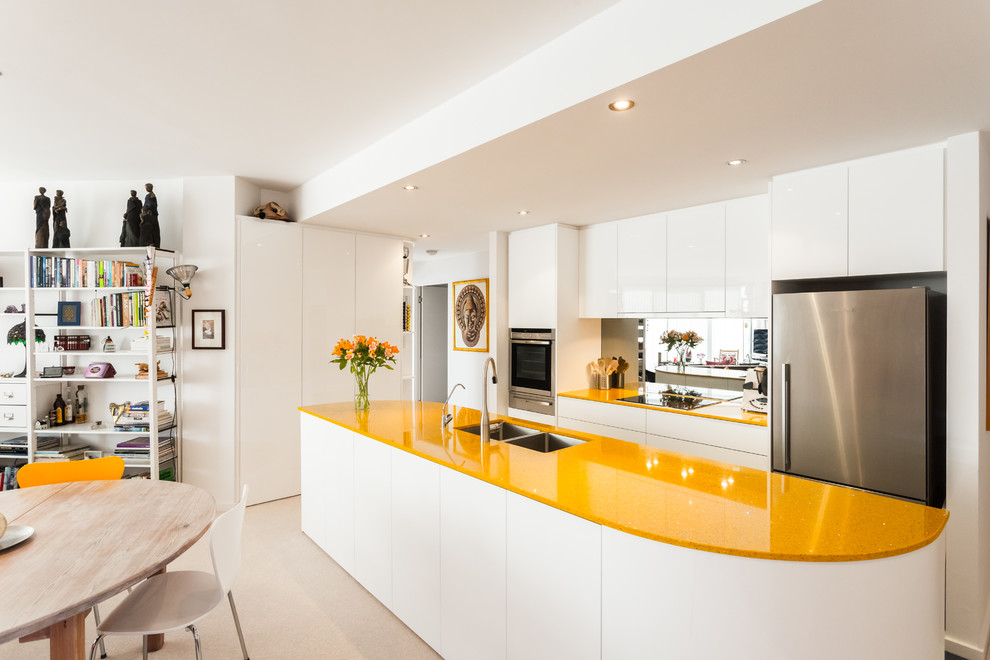 Inspiration for a small contemporary galley open plan kitchen in Perth with an undermount sink, flat-panel cabinets, white cabinets, metallic splashback, glass sheet splashback, stainless steel appliances, with island and recycled glass benchtops.