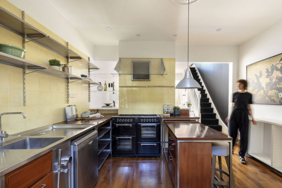 Contemporary l-shaped kitchen in Sydney with an integrated sink, open cabinets, stainless steel cabinets, stainless steel benchtops, yellow splashback, black appliances, medium hardwood floors and with island.