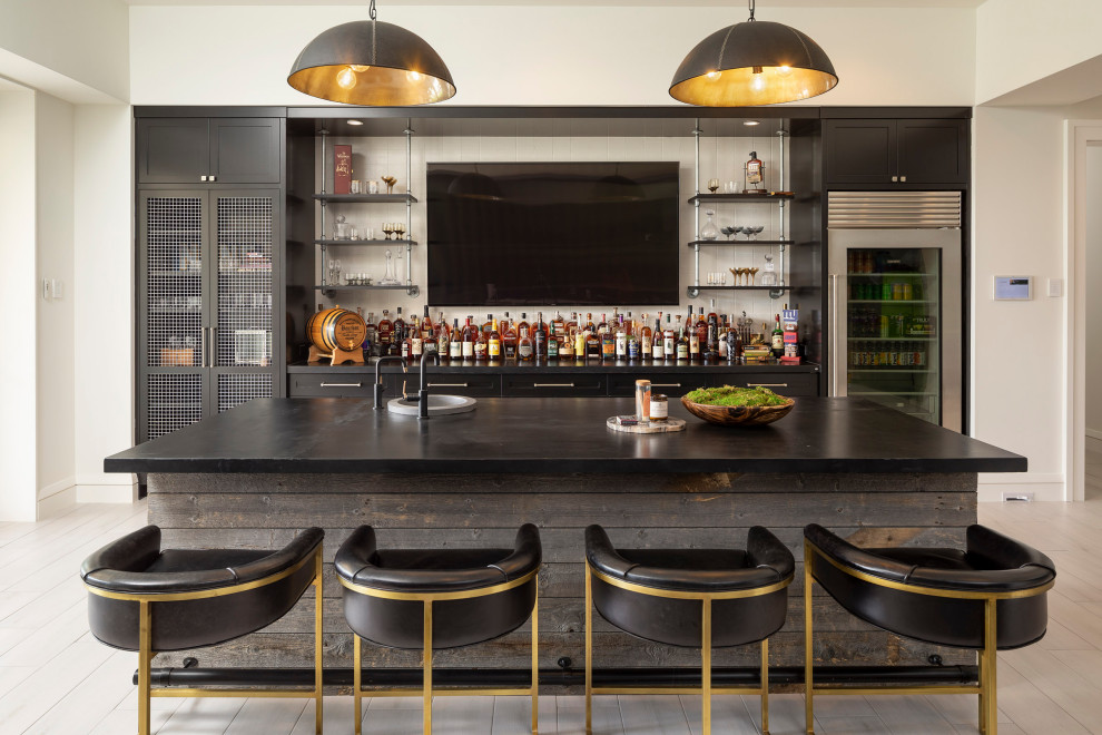 Photo of a transitional galley seated home bar in Minneapolis with a drop-in sink, shaker cabinets, black cabinets, quartz benchtops, white splashback, light hardwood floors, beige floor and black benchtop.