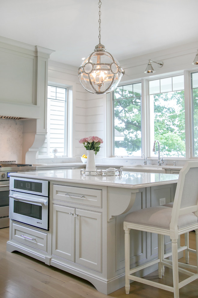 Design ideas for a large transitional u-shaped eat-in kitchen in Milwaukee with quartz benchtops, white splashback, with island, a farmhouse sink, light hardwood floors, beige floor, recessed-panel cabinets, white cabinets, stone slab splashback and panelled appliances.