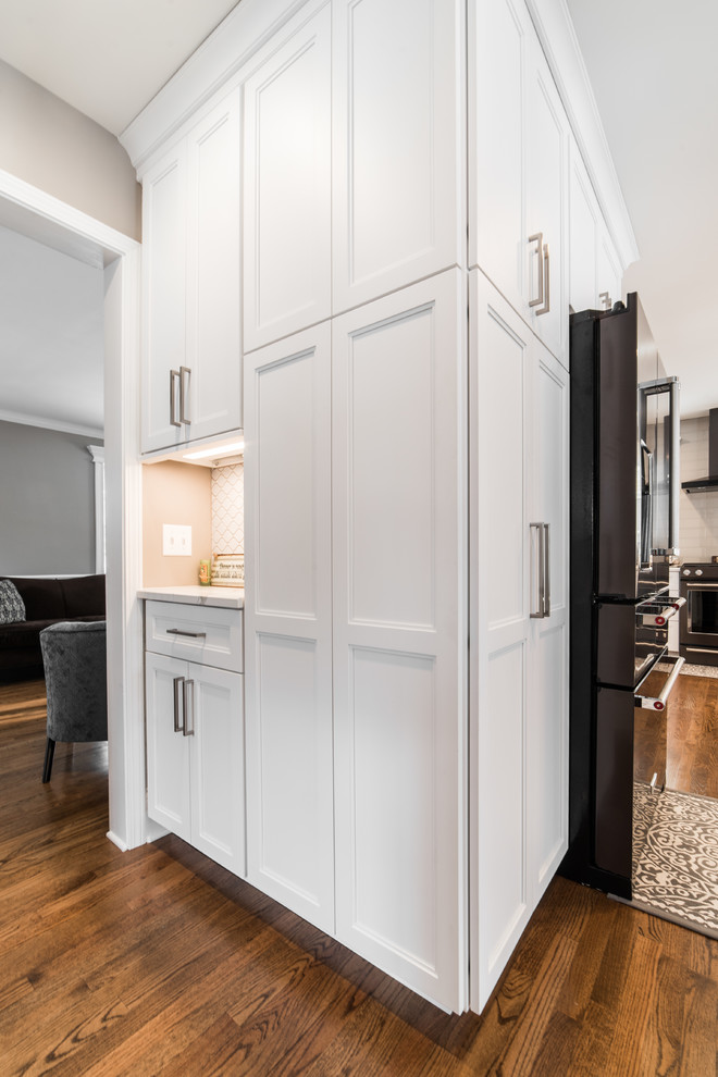 Inspiration for a mid-sized transitional l-shaped medium tone wood floor and brown floor eat-in kitchen remodel in Chicago with an undermount sink, recessed-panel cabinets, white cabinets, quartzite countertops, gray backsplash, subway tile backsplash, black appliances, no island and multicolored countertops