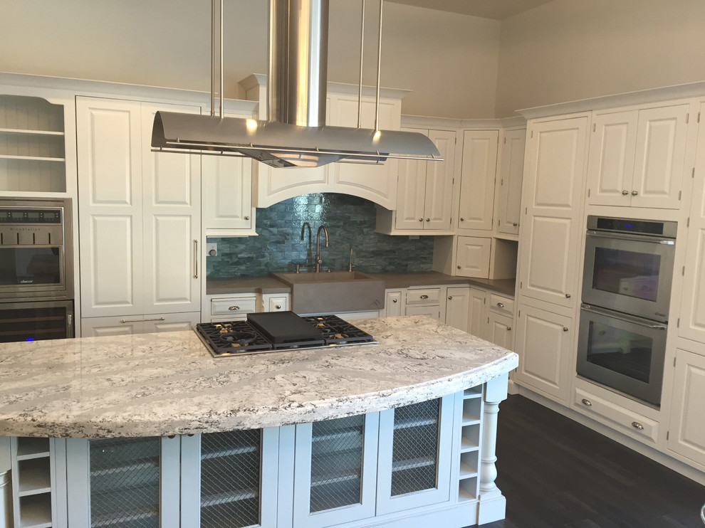 Photo of a large transitional l-shaped eat-in kitchen in Phoenix with a farmhouse sink, recessed-panel cabinets, white cabinets, green splashback, glass tile splashback, stainless steel appliances, vinyl floors, with island and concrete benchtops.