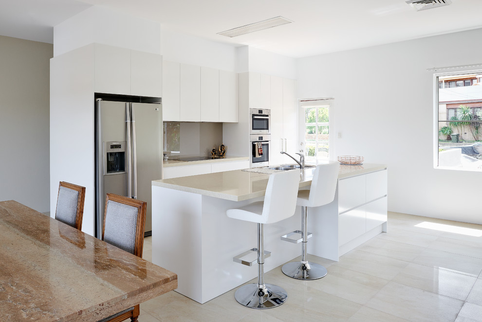 Design ideas for a mid-sized modern galley open plan kitchen in Sydney with a double-bowl sink, flat-panel cabinets, white cabinets, quartz benchtops, grey splashback, glass sheet splashback, stainless steel appliances, ceramic floors and with island.