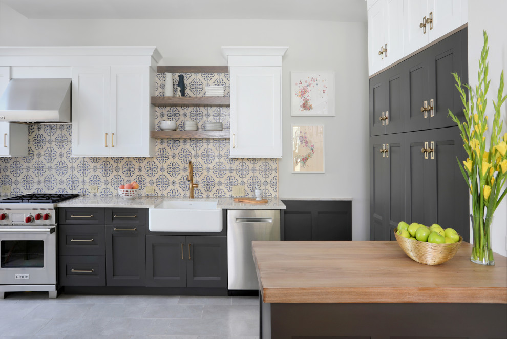 Inspiration for a mid-sized transitional u-shaped eat-in kitchen in Chicago with a farmhouse sink, recessed-panel cabinets, grey cabinets, wood benchtops, multi-coloured splashback, ceramic splashback, stainless steel appliances, porcelain floors, a peninsula, grey floor and brown benchtop.