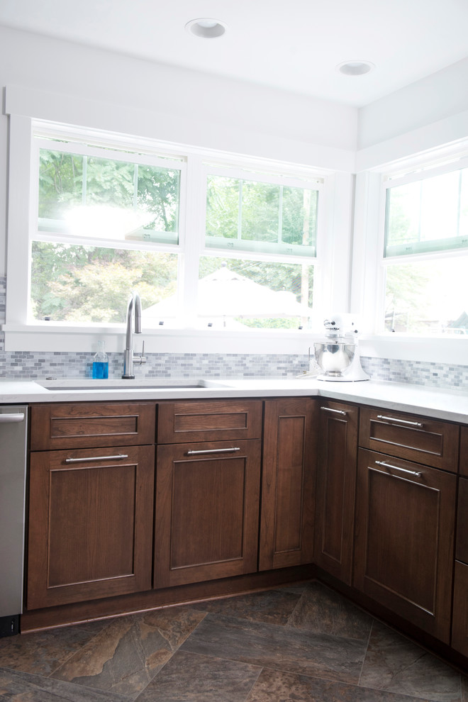 Example of a mid-sized transitional u-shaped vinyl floor and multicolored floor kitchen design with an undermount sink, shaker cabinets, brown cabinets, quartz countertops, gray backsplash, marble backsplash, stainless steel appliances, no island and white countertops