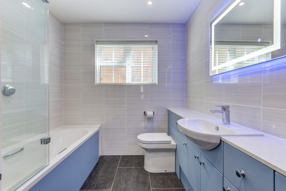 Cette image montre une salle de bain grise et blanche design de taille moyenne pour enfant avec un placard à porte plane, des portes de placard bleues, une baignoire en alcôve, un combiné douche/baignoire, WC suspendus, un carrelage beige, des carreaux de céramique, un mur beige, un lavabo intégré, un plan de toilette en stratifié, un sol gris, un plan de toilette blanc, meuble simple vasque et meuble-lavabo encastré.