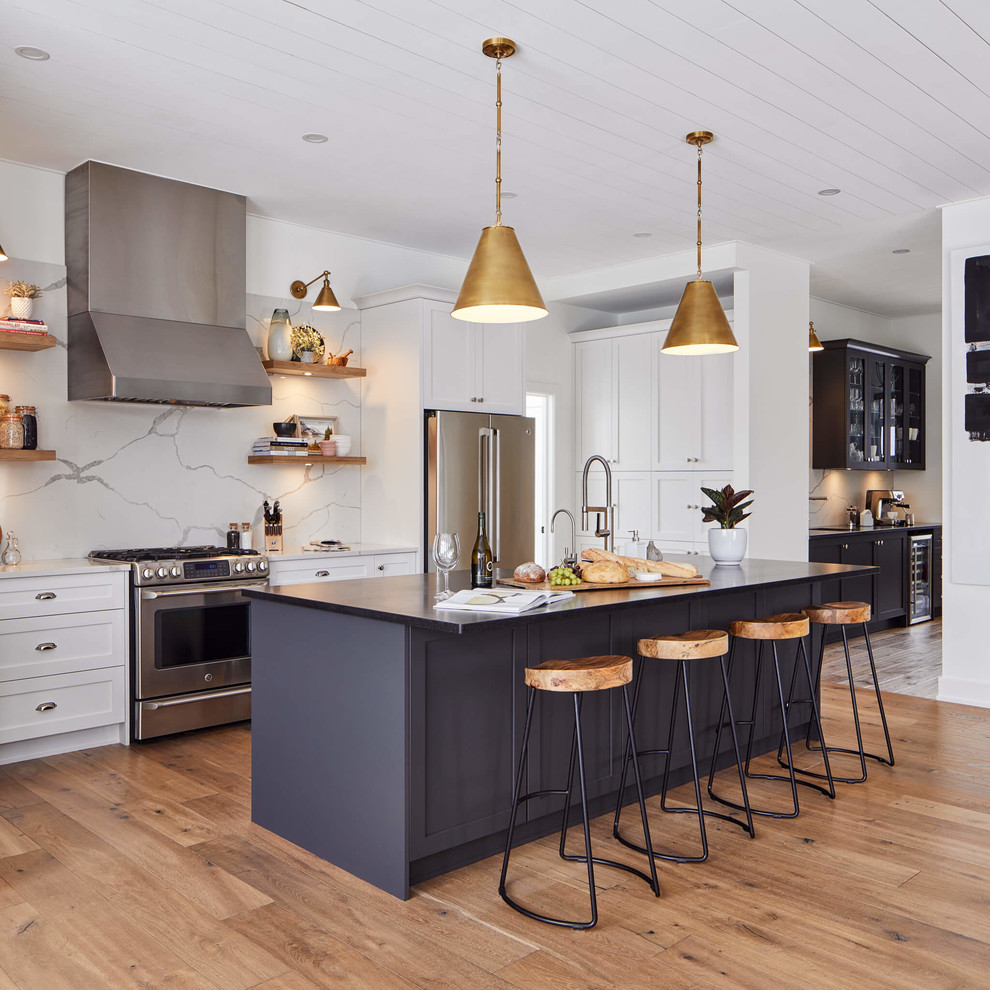 Inspiration for a large transitional light wood floor kitchen remodel in Ottawa with shaker cabinets, white cabinets, quartz countertops, white backsplash, stainless steel appliances, an island, white countertops and stone slab backsplash
