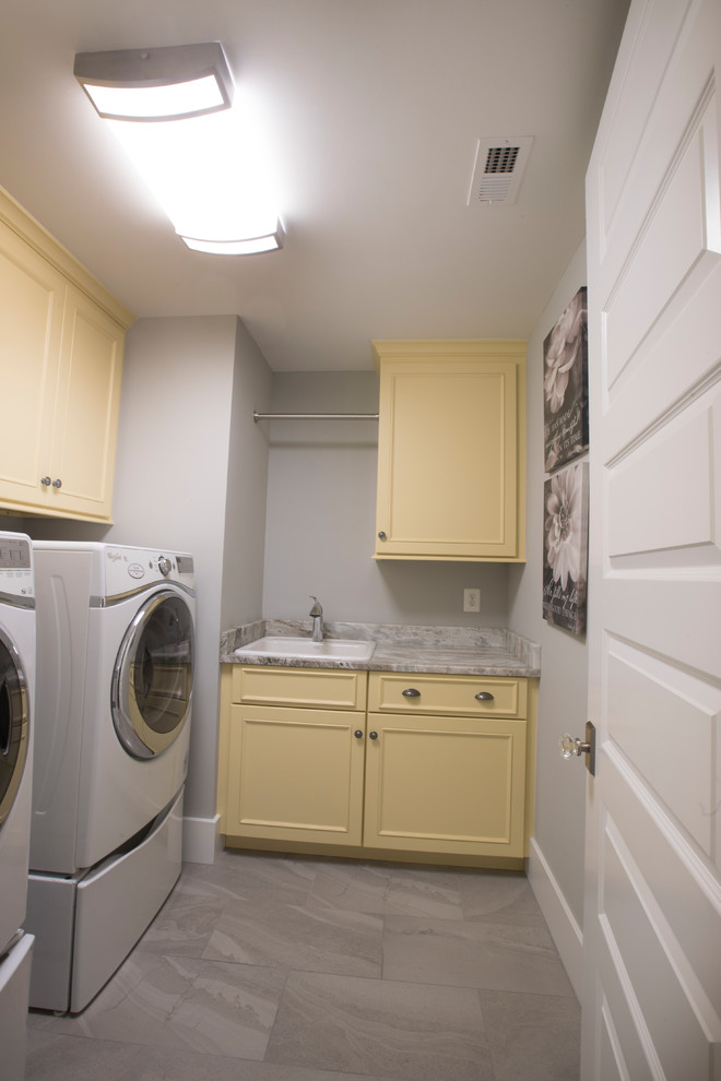 Inspiration for a mid-sized beach style l-shaped dedicated laundry room in Baltimore with a drop-in sink, recessed-panel cabinets, yellow cabinets, marble benchtops, grey walls, marble floors, a side-by-side washer and dryer, grey floor and grey benchtop.