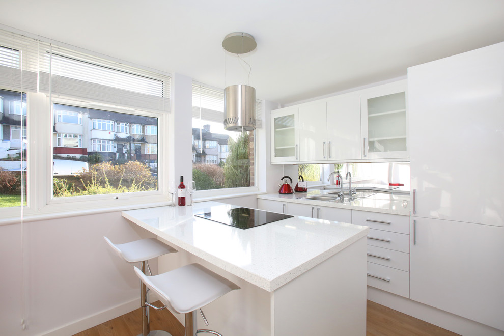 This is an example of a contemporary kitchen in London with an integrated sink, flat-panel cabinets, white cabinets, granite benchtops, mirror splashback, panelled appliances, laminate floors, with island, brown floor and yellow benchtop.