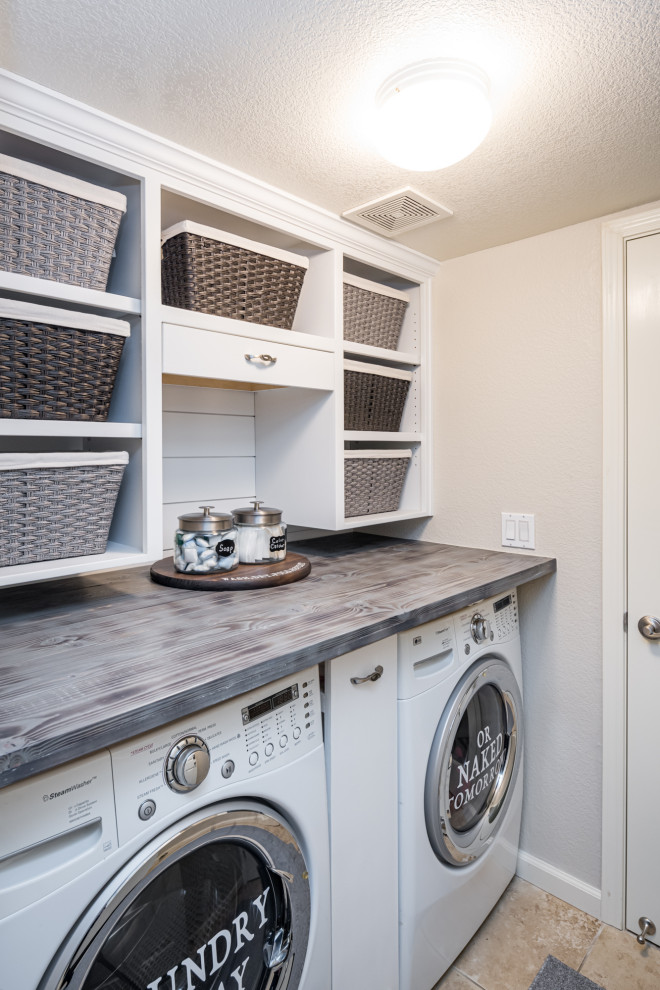 Inspiration for a small country single-wall utility room in Sacramento with open cabinets, white cabinets, wood benchtops, white walls, porcelain floors, a side-by-side washer and dryer, beige floor and grey benchtop.