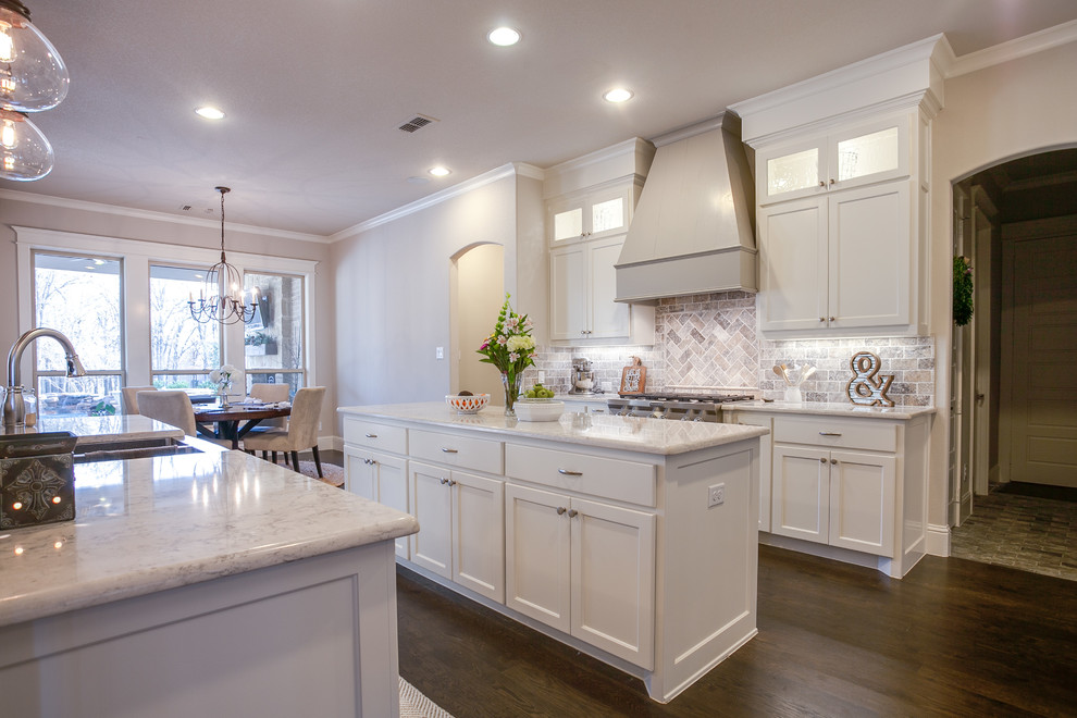 This is an example of a large country u-shaped open plan kitchen in Dallas with shaker cabinets, white cabinets, marble benchtops, grey splashback, stone tile splashback, stainless steel appliances, dark hardwood floors, multiple islands and a farmhouse sink.