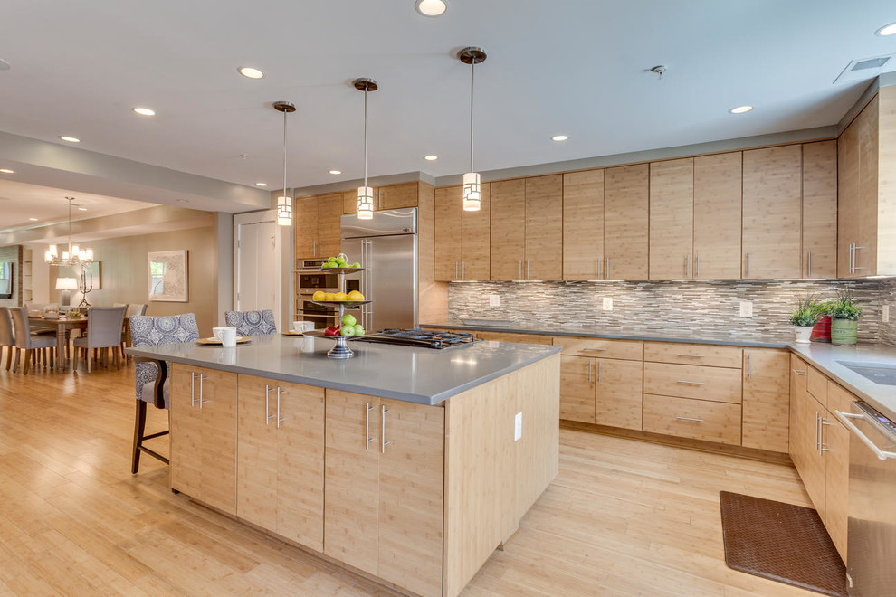 Photo of a mid-sized modern l-shaped eat-in kitchen in DC Metro with flat-panel cabinets, light wood cabinets, quartz benchtops, grey splashback, mosaic tile splashback, stainless steel appliances, bamboo floors, with island and grey benchtop.