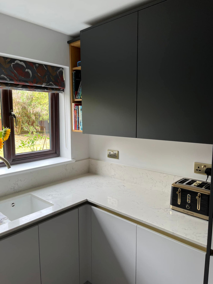Photo of a mid-sized modern galley separate kitchen in Other with a drop-in sink, flat-panel cabinets, grey cabinets, quartzite benchtops, white splashback, engineered quartz splashback, black appliances, vinyl floors, no island, brown floor and white benchtop.