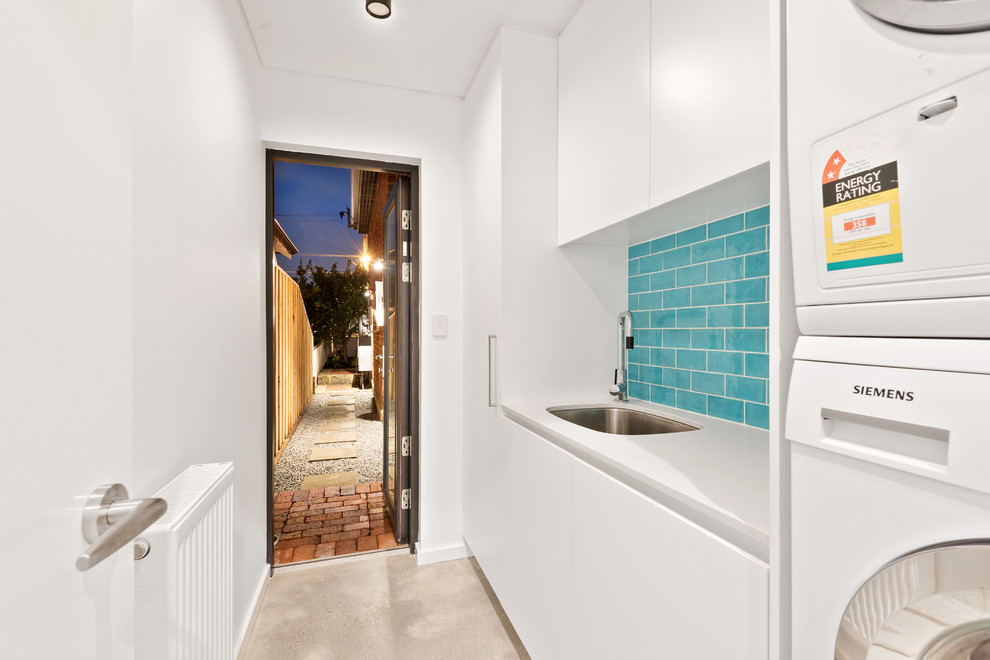 Country single-wall dedicated laundry room in Perth with an utility sink, flat-panel cabinets, white cabinets, white walls, concrete floors, a stacked washer and dryer, grey floor and white benchtop.