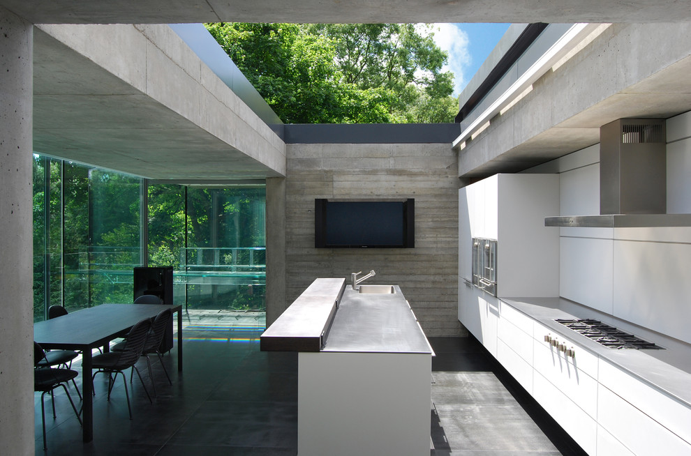 Photo of a mid-sized contemporary single-wall eat-in kitchen in London with a drop-in sink, flat-panel cabinets, white cabinets, stainless steel benchtops, white splashback, panelled appliances and with island.